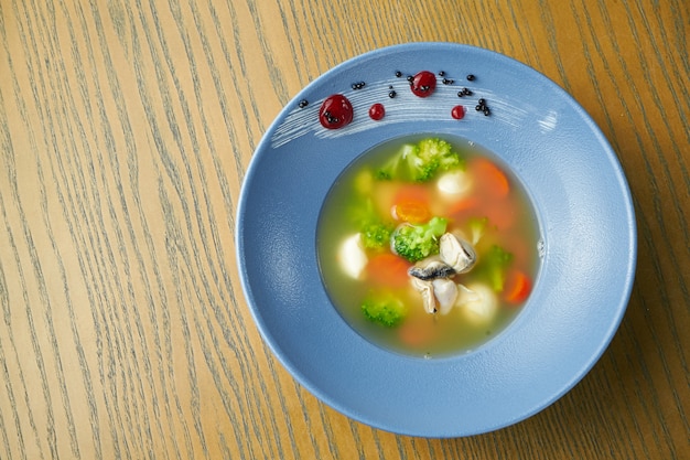 Smakelijke zeevruchtensoep. Bouillon met mosselen, wortelen, broccoli en sint-jakobsschelpen in een blauw bord op een houten oppervlak