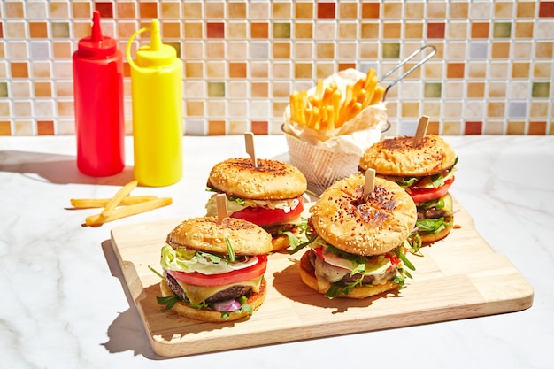 Smakelijke zelfgemaakte hamburgers op houten snijplank met fel zonlicht hamburger met kalfskoteletten pamidorom kaas rode ui sla rucola salade en frietjes fastfood concept