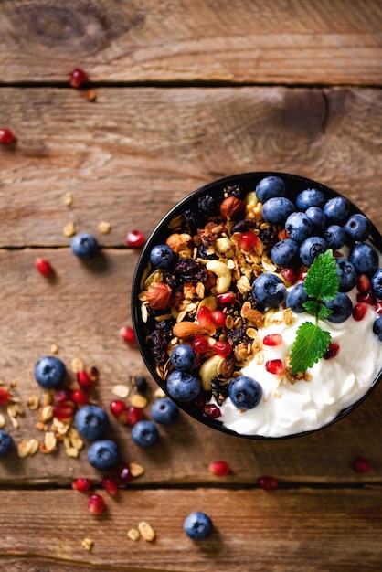 Smakelijke zelfgemaakte muesli, yoghurt, verse biologische bessen, granaatappel, mint op rustieke houten met kopie ruimte, bovenaanzicht.