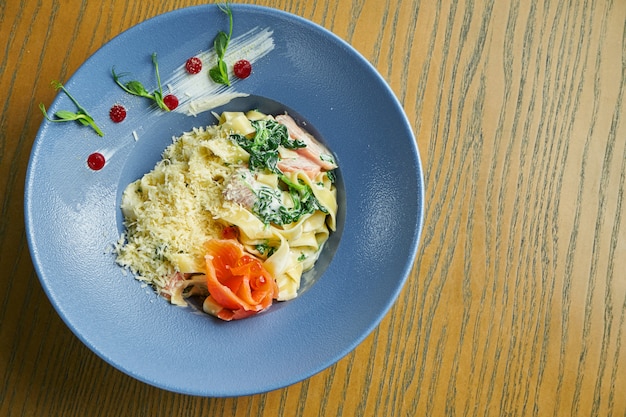 Smakelijke, zelfgemaakte tagliatelle pasta met spinazie en zalm, Parmezaanse kaas in een blauwe kom op een houten oppervlak. Italiaanse keuken. Voeg ruis toe aan post. Selectieve aandacht