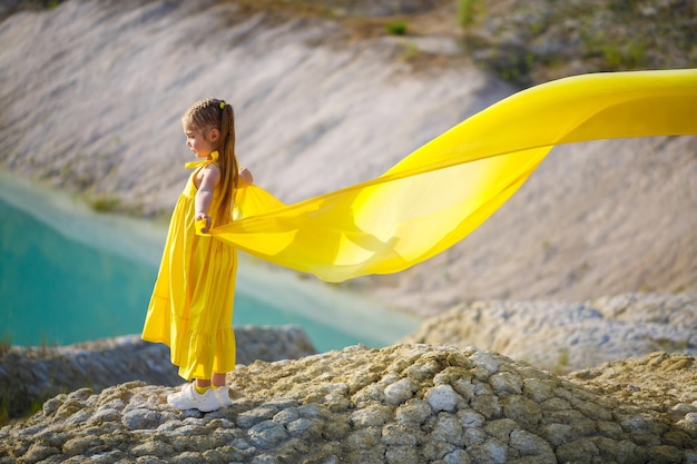 A small 67 years old Ukrainian girl in a yellow dress with wings in yellow fabric by the lake Blue sky and yellow fabric the colors of the Ukrainian flag