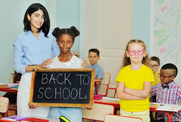 Small africanamerican school girl smiles and holds a sign that says back to school next to a female ...