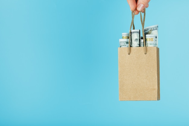 Una borsa per piccoli aiuti fatta di carta in una mano tesa con dollari usa su sfondo blu. layout del modello di packaging con spazio per la copia, la pubblicità.