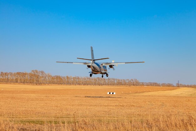 A small aircraft for the transport of passengers and paratroopers lands in a field on a landing strip with grass under a blue sky above the trees on a clear cloudless day Air patrol