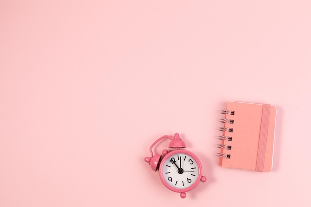 Small alarm clock and clean notebook pastel pink background