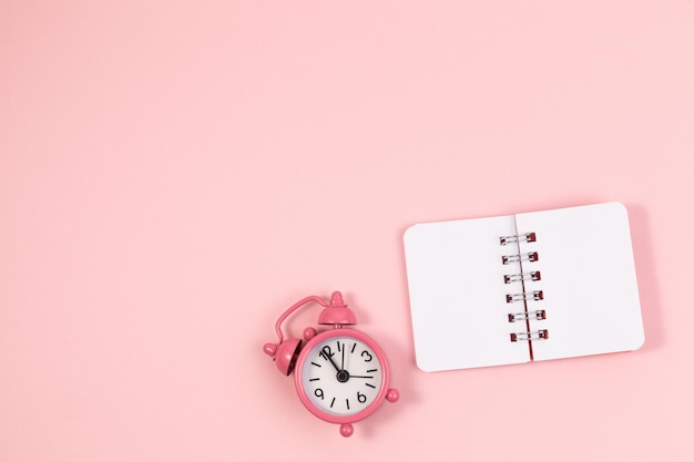 Small alarm clock and clean notebook pastel pink background