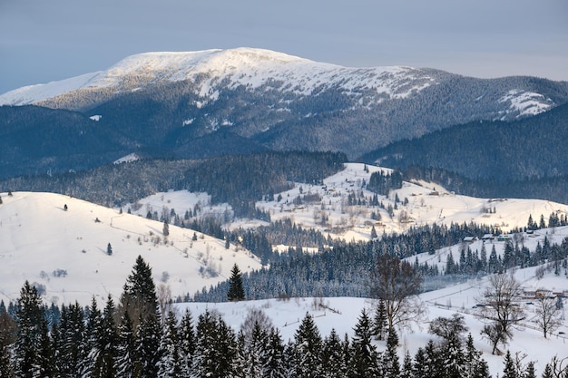 Small alpine village and winter snowy mountains in first sunrise sunlight around Voronenko Carpathian Ukraine