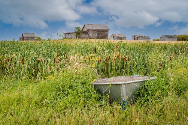 Small aluminium boat with an abandoned home in a farmyard on the Canadian prairies