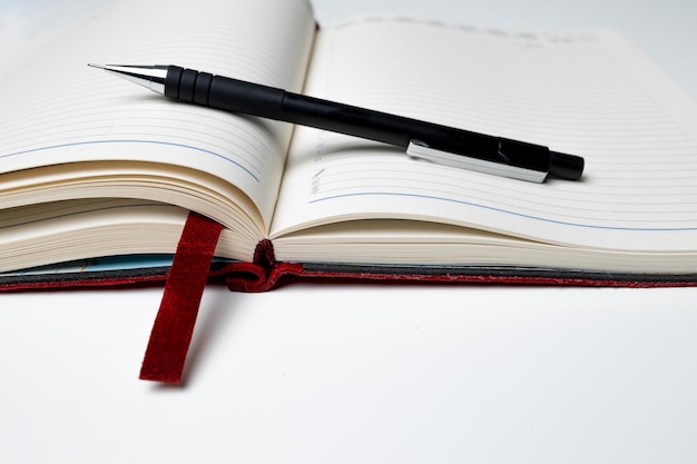 A small angle of a black pen lying on a red open diary on the table