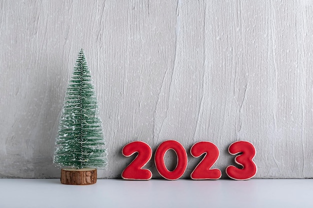 Small artificial Christmas tree and red numbers 2023 against a gray wall New year concept Copy space