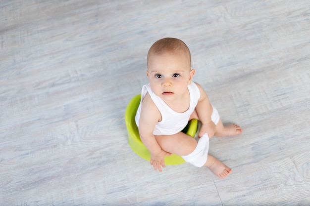 Small baby boy 8 months old sitting on a potty, baby toilet