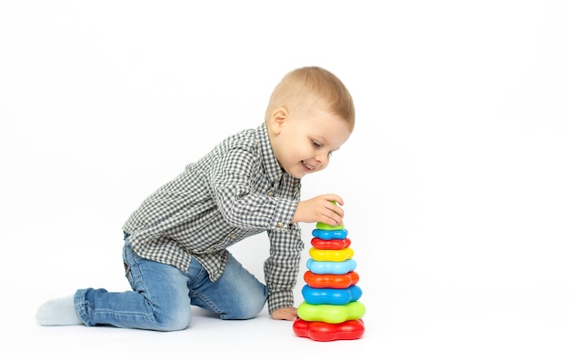 Small baby boy is playing with colourfull pyramide isolated on white surface