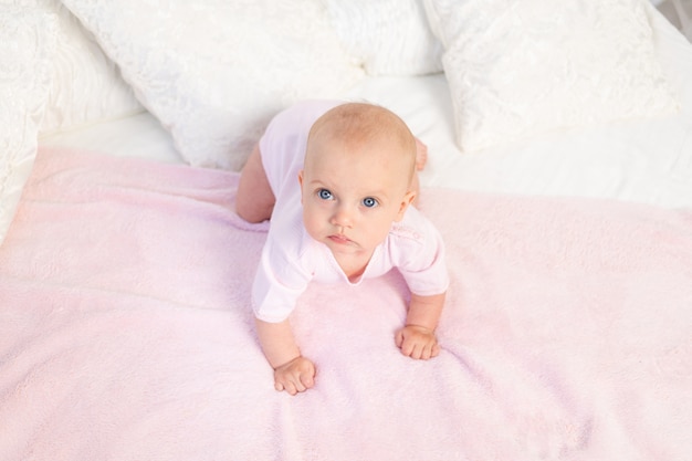 6 개월 된 작은 아기 소녀 집에서 흰색과 분홍색 침대에서 크롤링, 멀리보고, 상위 뷰