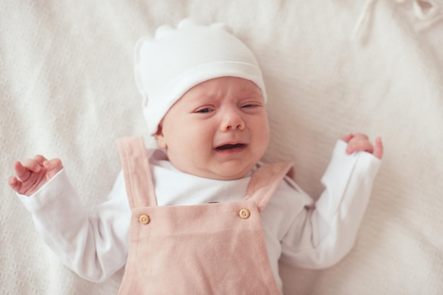 Small baby girl crying lying in bed over white