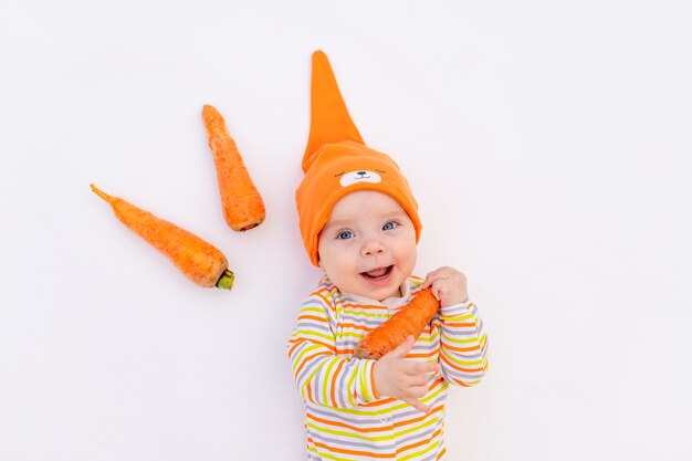 Small baby girl six months old lying on a white isolated with a carrot 