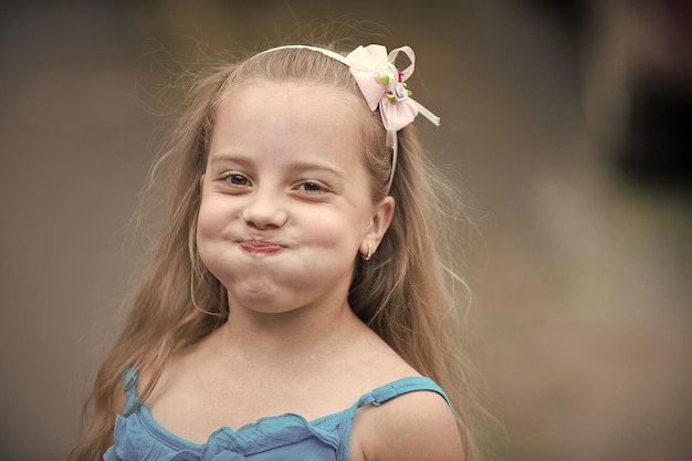 Маленькая девочка с улыбающимся лицом в синем жилете на открытом воздухе