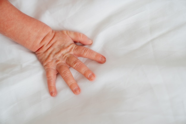 A small baby hand on a white sheet.