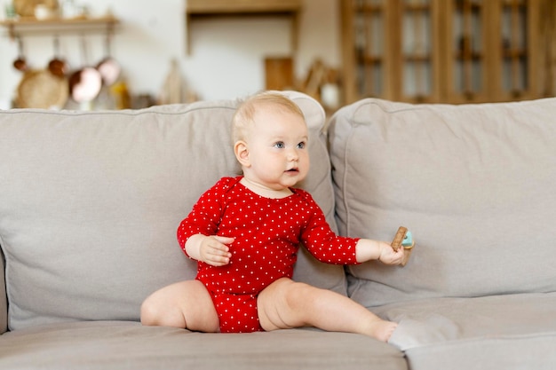 작은 아름다운 아기가 집에서 거실에서 소파에 앉아 빨간 옷을 입은 귀여운 아이