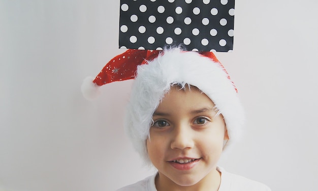 A small beautiful  boy in a Santa Claus with a gift on his head . The concept of Merry Christmas