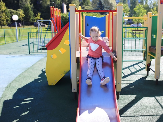 A small beautiful girl, rolls on a hill on a children's playground.