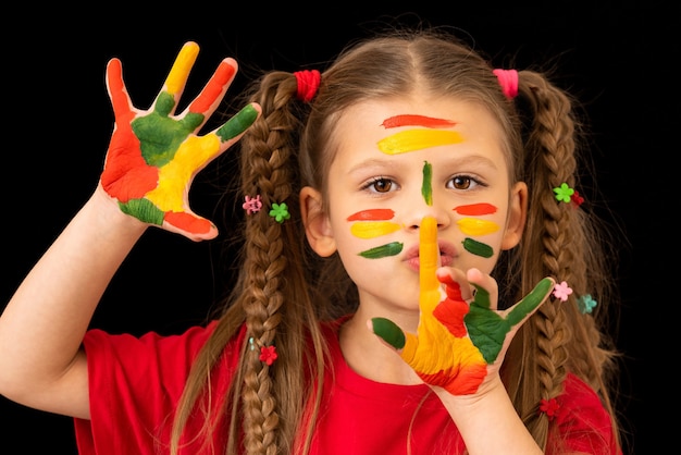 A small beautiful girl with pigtails holds her finger near her lips.