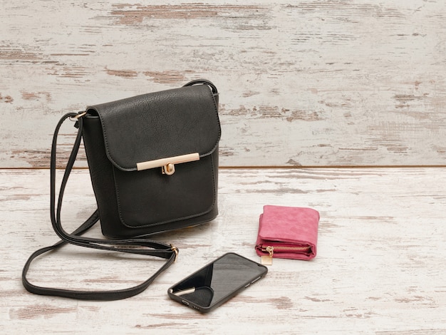 Small black female handbag, purse and phone on a wooden background. Fashionable concept