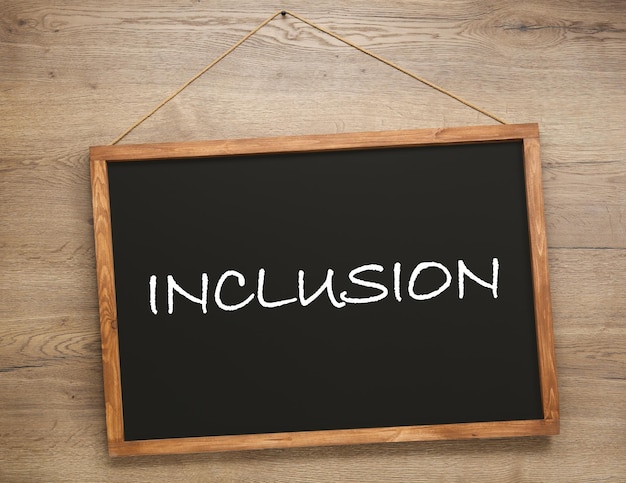 木製の壁にぶら下がっている「INCLUSION」という言葉が書かれた小さな黒板