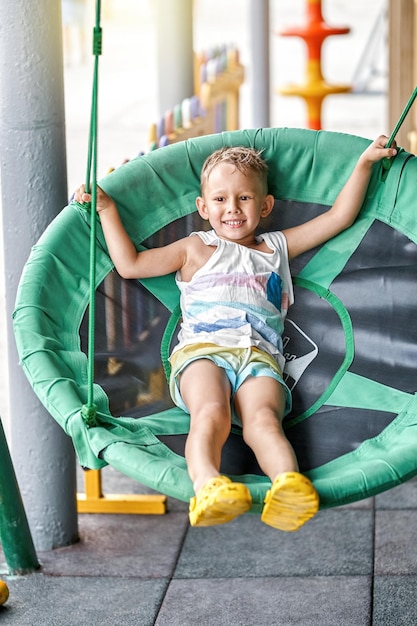 Small blond boy sits in green swing armchair at coastal resort