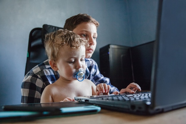 A small blond child with a pacifier in his brother's arms sits at the computer and holds a graphic tablet