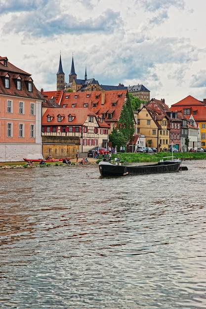 Маленькая лодка, дома рыбаков и река Регниц в Маленькой Венеции Бамберга в Верхней Франконии, Бавария, Германия. Люди на заднем плане
