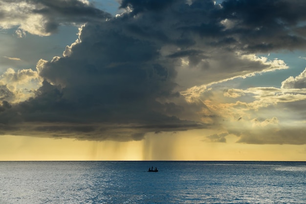 Small boat sailing in a calm sea and with the storm and clouds approaching on the horizon