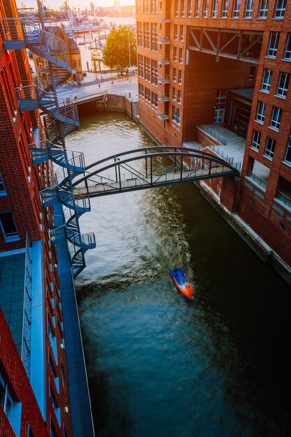 写真 古い倉庫地区の赤いレンガの建物間の運河を渡る橋の下の小さなボート