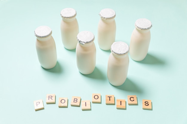 Small bottles with probiotics and prebiotics dairy drink on blue background. Production with biologically active additives. Fermentation and diet healthy food. Bio yogurt with useful microorganisms.