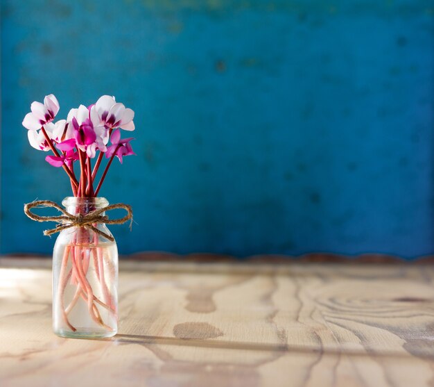 A small bouquet of flowers of cyclamen in a glass bottle on a wooden