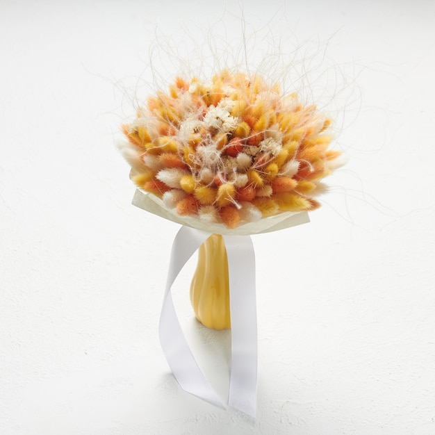 写真 白地に花瓶に立っている白とオレンジのラグルスの小さな花束