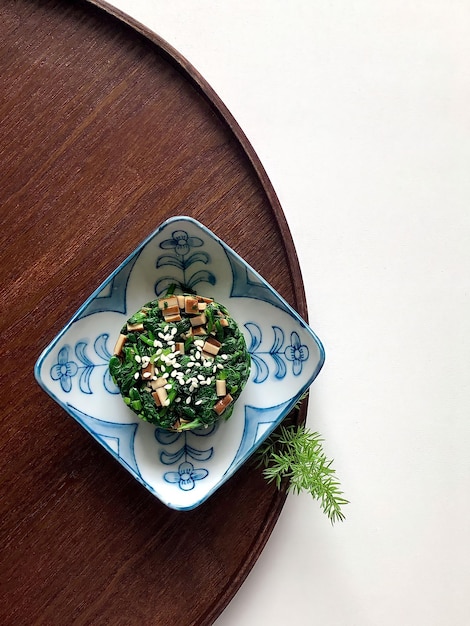 A small bowl of green food with sesame seeds on top.