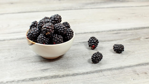 Small bowl with blackberries on gray wood desk.