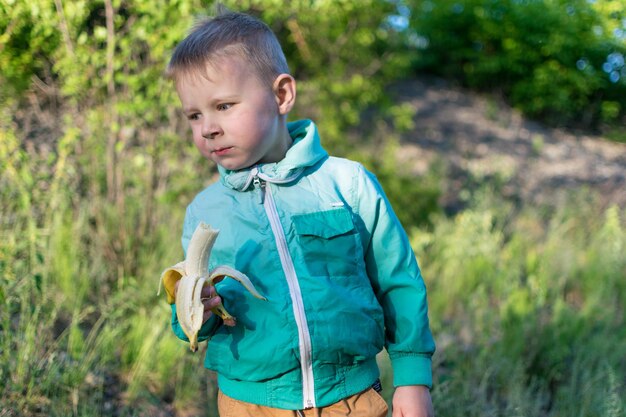 35歳の小さな男の子が新鮮な空気の中を散歩中に自然の中でバナナを食べていますスナック