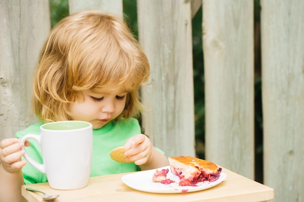 Photo small boy eating pie near wooden fence