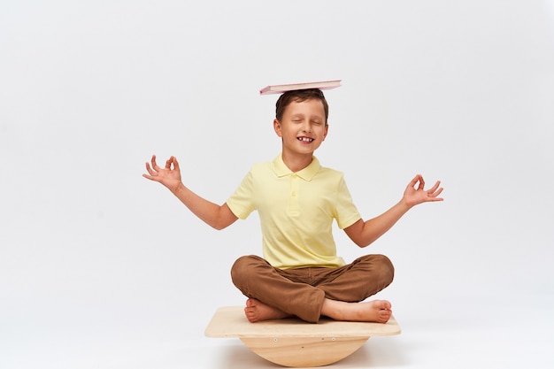 Photo small boy holds book on his head while balancing on special simulator