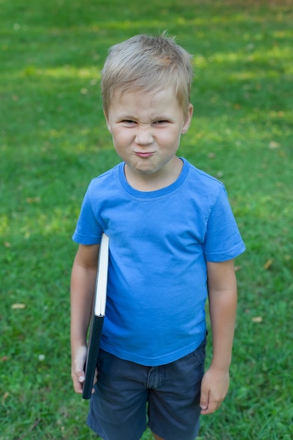 small boy in the Park stands and holds a book in his hands.