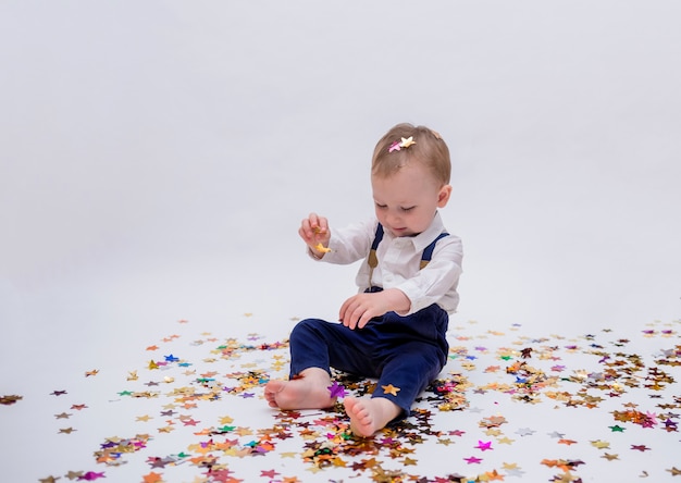 small boy sits and plays with confetti on a white isolated