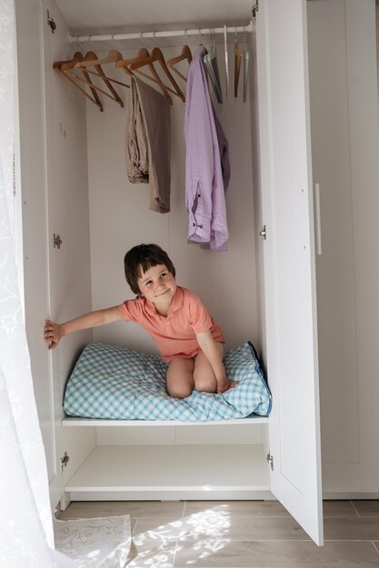 Photo small boy sitting in a wardrobe and looking out of the door