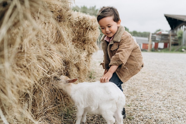 Small boy wearing stylish clothes playing with goat