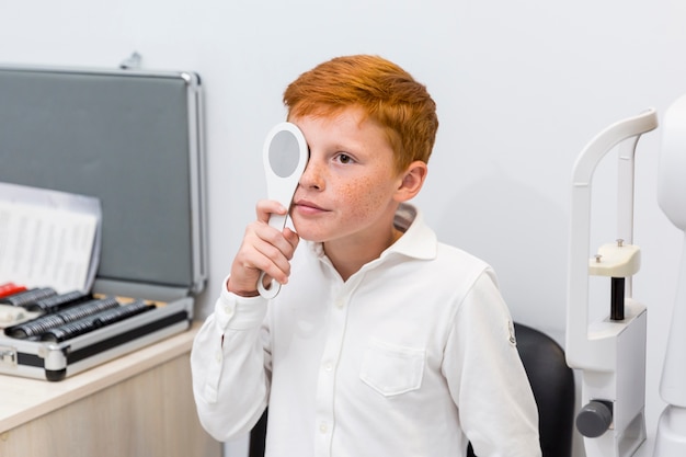 Il bambino piccolo in camicia bianca ha coperto il suo occhio di occluder nella clinica di ottica