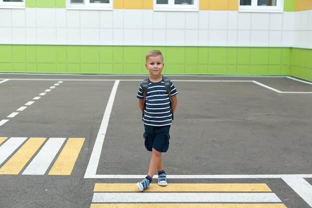 A small boy with a backpack, crossing the road alone near the school