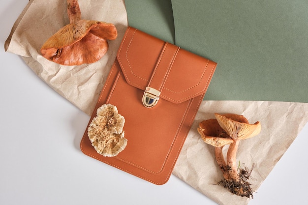 Small brown bag and poisonous toadstools on a green background, eco-leather from mushroom mycelium concept, natural textiles, vegan leather from natural recyclable materials