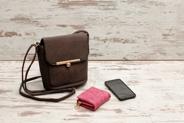 Small brown female handbag, purse and phone on a wooden . Fashionable 