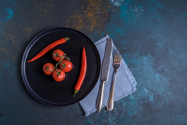 Piccolo mazzo di pomodori e di peperoncini freschi maturi sulla banda nera, disposizione piana.