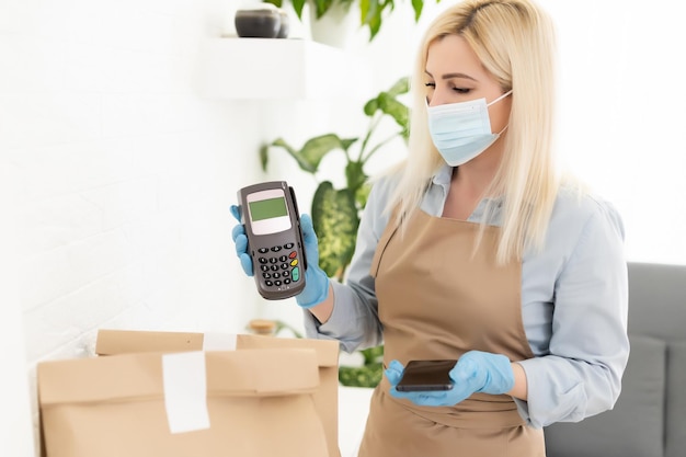 Small business, coronavirus, social distancing and contactless payment concept. barista, waitress in cafe, medical mask and gloves, recommend use POS terminal for safe purchase during covid-19.